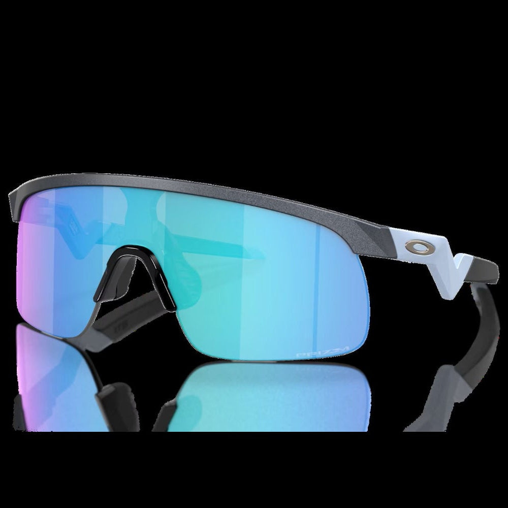 Oakley shield-style sunglasses with a matte black frame and large mirrored lenses showing a blue-to-purple gradient, photographed on a black background with a reflection below.